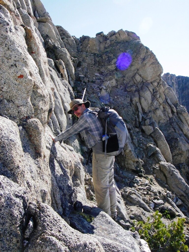 The 3rd class ledge/ramp. Carl is pointing to its terminus; here we roped up to climb about 15 feet up left to the black dike. Judi Steciak Photo